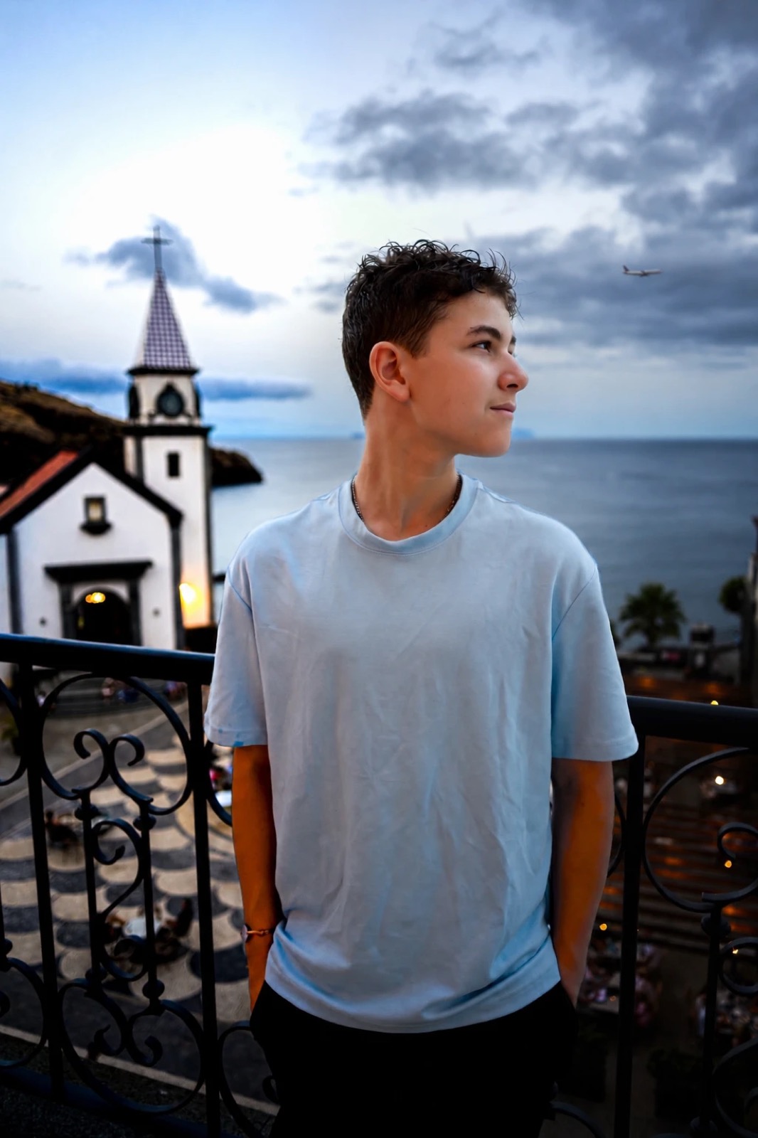 Ethan Paschkes on a balcony by the sea, an airliner passing overhead